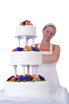 Baker lady giving to a wedding cake latest proud look in her apron and white bandanna, cake has fondant ruffles on the side and decorated with orange and purple gum paste roses