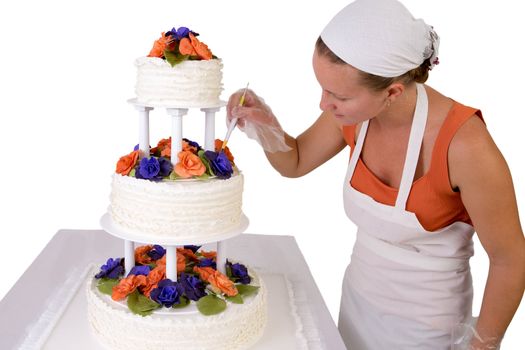 Baker lady with a white bandanna giving to a wedding cake final touchups, cake has fondant ruffles on the side and decorated with orange and purple gum paste roses