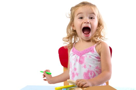 Toddler girl learning at the table very excidted , her eyebrowns are raised and mouth opened large holding colorful markers