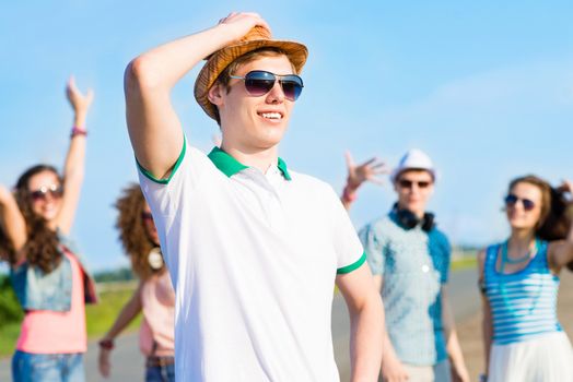 young man in sunglasses, a hat holds a hand on a background of blue sky and friends