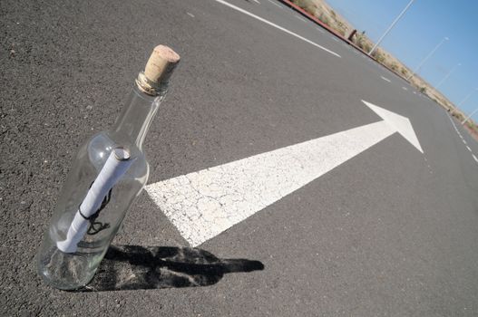 Message on a bottle and arrow on a asphalt street to the future