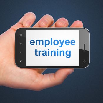 Education concept: hand holding smartphone with word Employee Training on display. Mobile smart phone in hand on Dark Blue background.