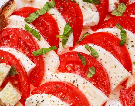 Tomato and mozzarella slices decorated with basil leaves on a plate 