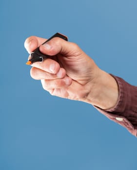 Hand holding a orange marker on blue background