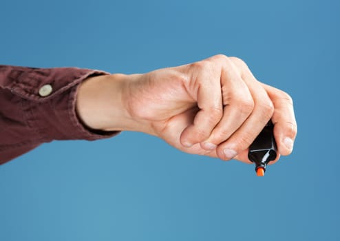 Hand holding a orange marker on blue background