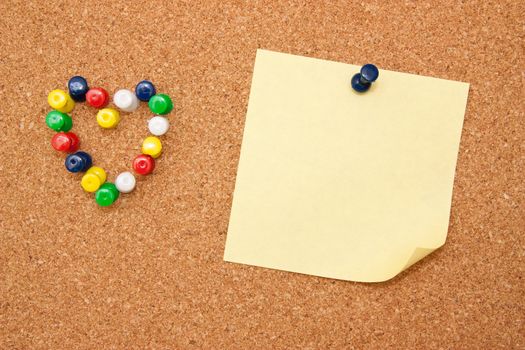 Corkboard with pushpins as heart and yellow note