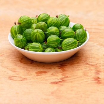 White Dish Filled With Succulent Juicy Fresh Ripe Green Gooseberries On An Old Wooden Table Top.