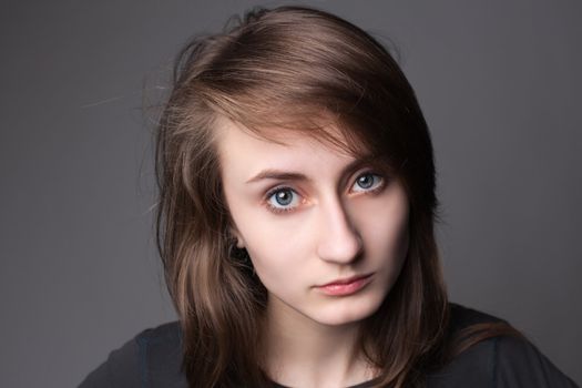 Closeup portrait of a lovely young female model looking confidently against grey background