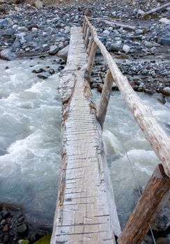 A narrow log is set up as a foot bridge over the rushing water of the Nisqually River at Mount Rainier National Park.