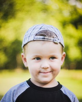 Happy caucasian child boy smiling outdoors with stripped cap, green nature background