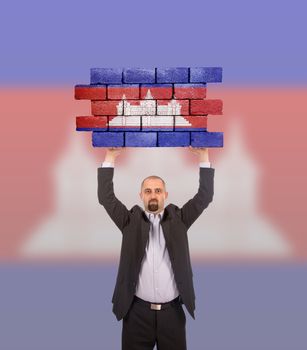 Businessman holding a large piece of a brick wall, flag of Cambodia, isolated on national flag