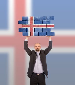 Businessman holding a large piece of a brick wall, flag of Iceland, isolated on national flag
