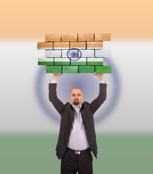 Businessman holding a large piece of a brick wall, flag of India, isolated on national flag