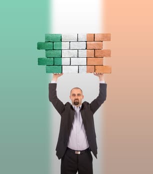 Businessman holding a large piece of a brick wall, flag of Ireland, isolated on national flag