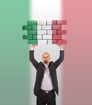 Businessman holding a large piece of a brick wall, flag of Italy, isolated on national flag