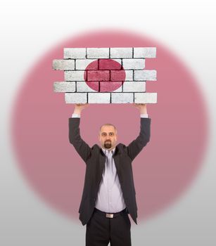 Businessman holding a large piece of a brick wall, flag of Japan, isolated on national flag