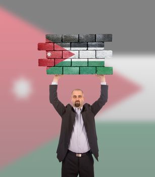 Businessman holding a large piece of a brick wall, flag of Jordan, isolated on national flag