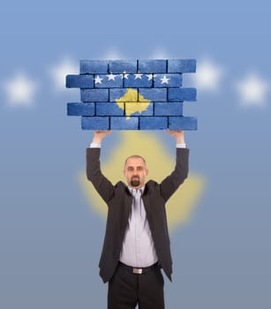 Businessman holding a large piece of a brick wall, flag of Kosovo, isolated on national flag