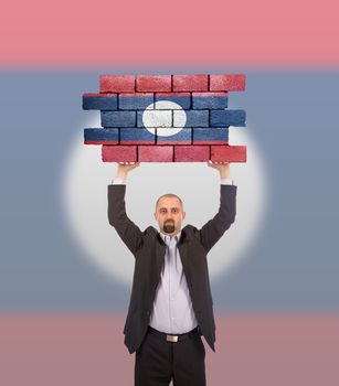 Businessman holding a large piece of a brick wall, flag of Laos, isolated on national flag