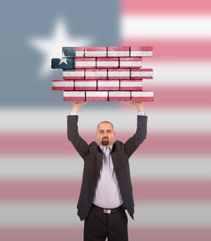 Businessman holding a large piece of a brick wall, flag of Liberia, isolated on national flag