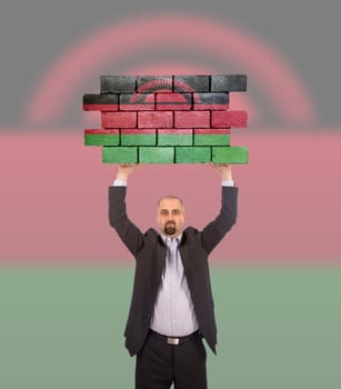 Businessman holding a large piece of a brick wall, flag of Malawi, isolated on national flag