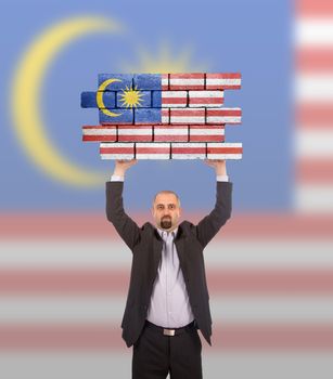 Businessman holding a large piece of a brick wall, flag of Malaysia, isolated on national flag