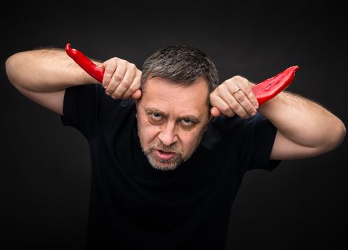 An elderly man holding two red hot chili peppers near the head like horns