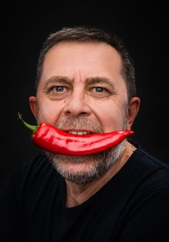 Portrait of elderly man with red pepper in his mouth