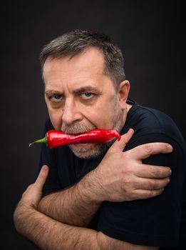 Portrait of elderly man with red pepper in his mouth