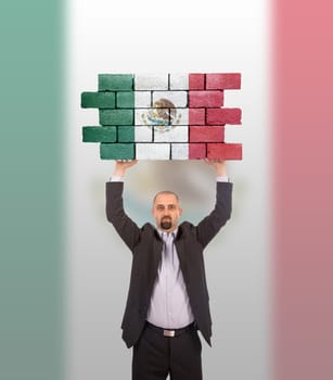 Businessman holding a large piece of a brick wall, flag of Mexico, isolated on national flag