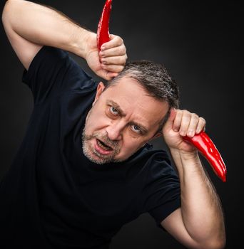 An elderly man holding two red hot chili peppers near the head like horns