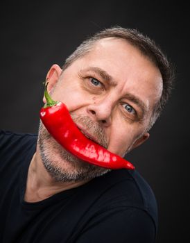 Portrait of elderly man with red pepper in his mouth