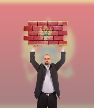 Businessman holding a large piece of a brick wall, flag of Montenegro, isolated on national flag