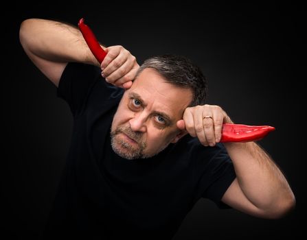 An elderly man holding two red hot chili peppers near the head like horns