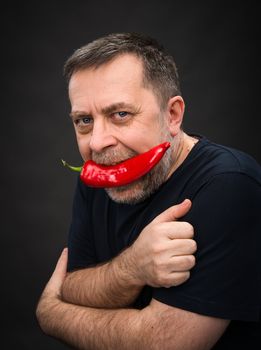 Portrait of elderly man with red pepper in his mouth