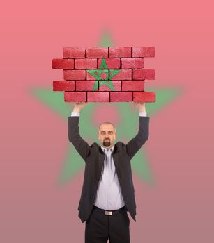 Businessman holding a large piece of a brick wall, flag of Morocco, isolated on national flag