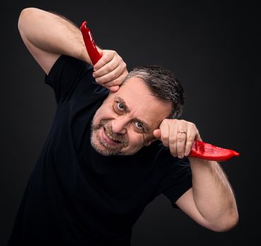 An elderly man holding two red hot chili peppers near the head like horns