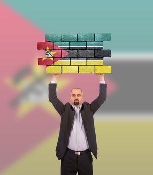 Businessman holding a large piece of a brick wall, flag of Mozambique, isolated on national flag