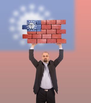 Businessman holding a large piece of a brick wall, flag of Myanmar, isolated on national flag