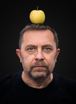 Portrait of a middle-aged man with a green apple on his head