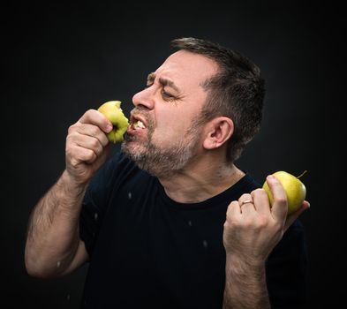 Middle-aged man in black with an appetite eating a green apple