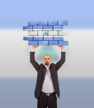 Businessman holding a large piece of a brick wall, flag of Nicaragua, isolated on national flag