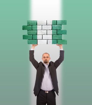 Businessman holding a large piece of a brick wall, flag of Nigeria, isolated on national flag