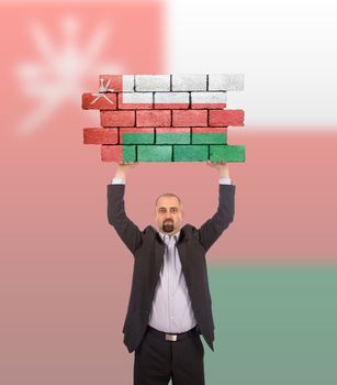 Businessman holding a large piece of a brick wall, flag of Oman, isolated on national flag