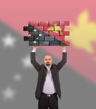 Businessman holding a large piece of a brick wall, flag of Papua New Guinea, isolated on national flag