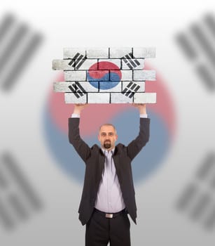 Businessman holding a large piece of a brick wall, flag of South Korea, isolated on national flag