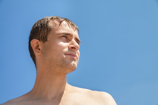 Portrait of a wet young man on blue sky background