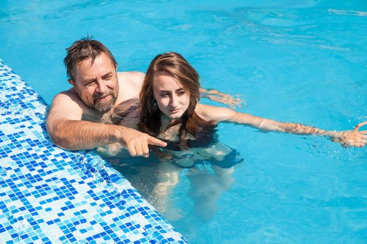 Happy family. Father and daughter swimming in the pool on a sunny day.