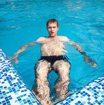 Healthy lifestyle. The young man is swimming in a pool on a sunny day