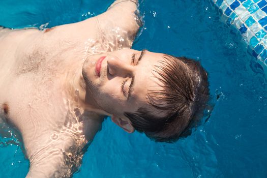 Healthy lifestyle. The young man is swimming in a pool on a sunny day